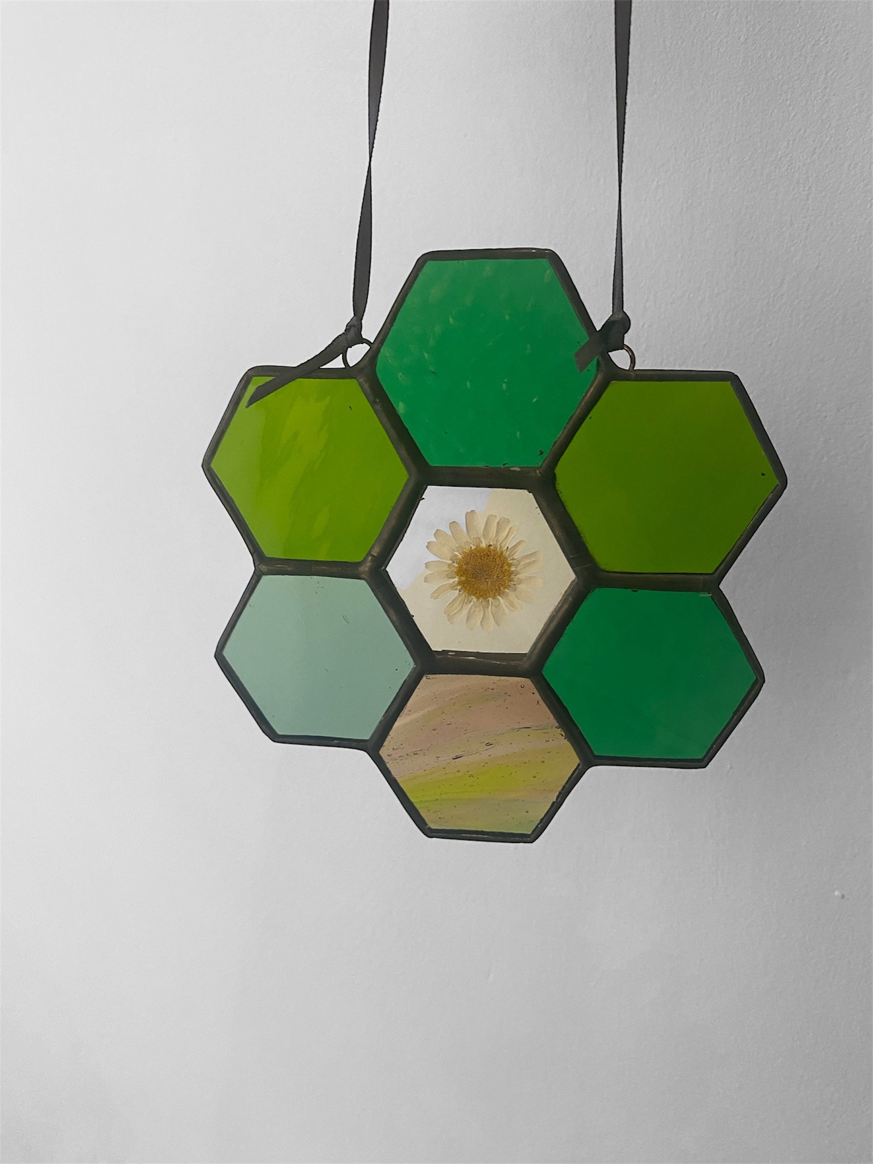 Hexagonal green stained glass piece with a dried flower daisy on a white background