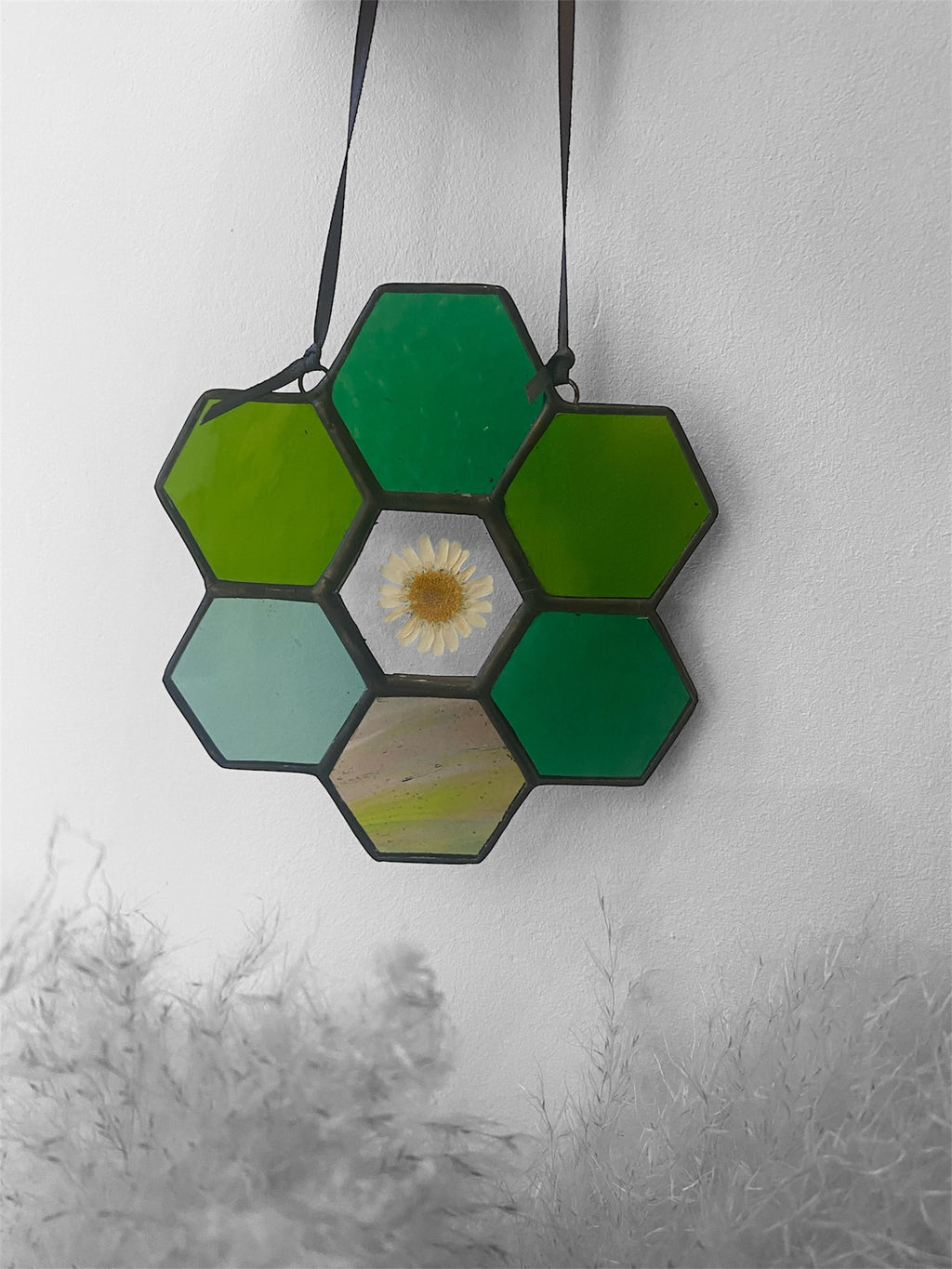 Hexagonal green stained glass piece with a dried flower daisy on a white background