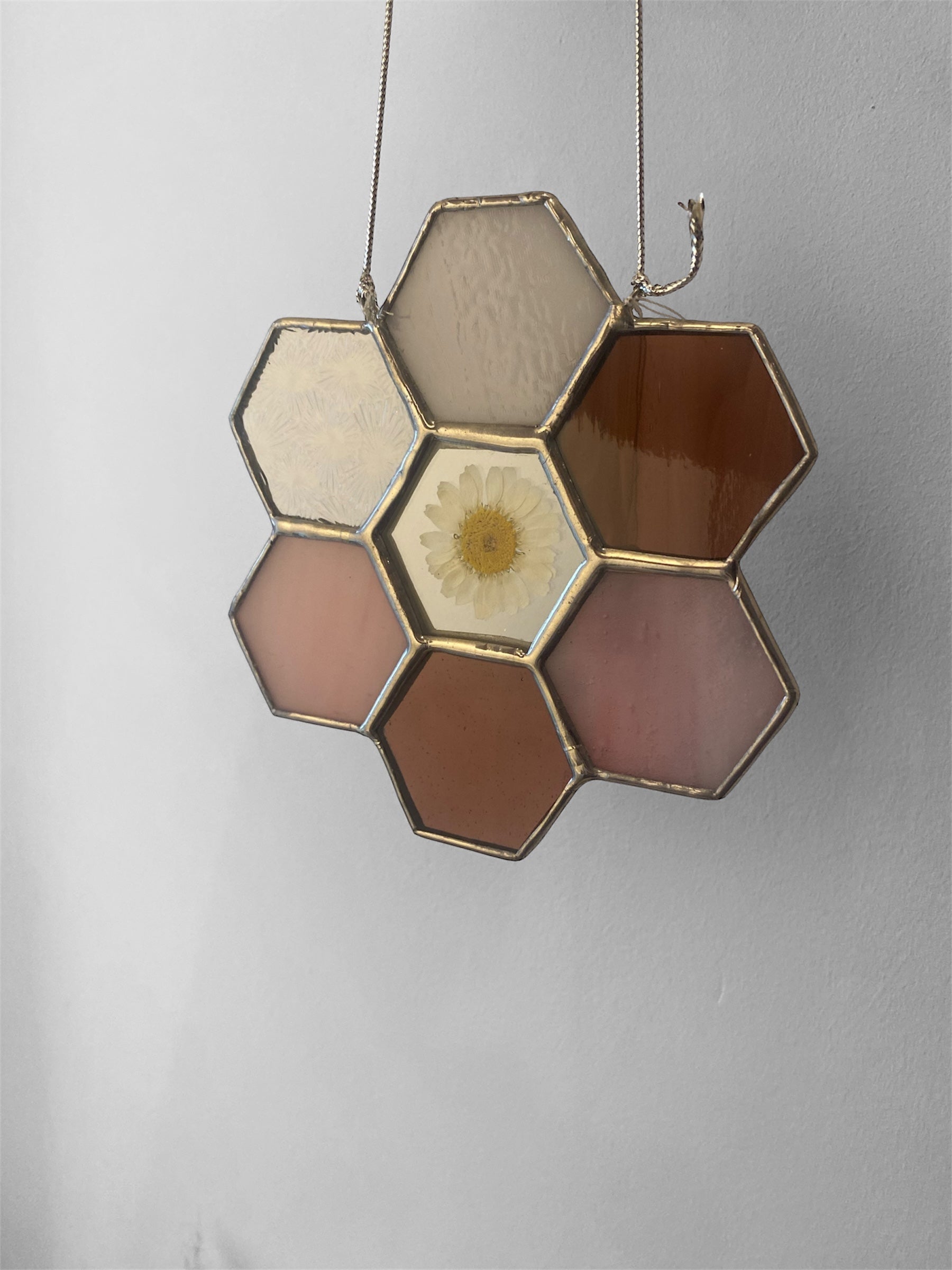 Hexagonal pink stained glass panel with a central floral daisy design on a plain background