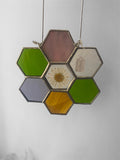 Hexagonal green and purple stained glass panel with floral daisy center on a plain background